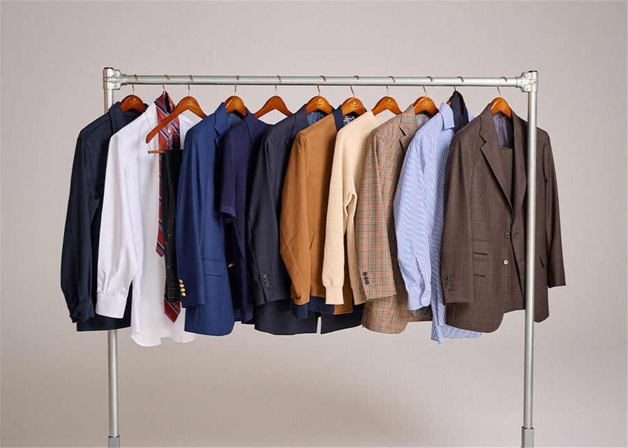 Clothing rack with various jackets and shirts on hangers against a plain background